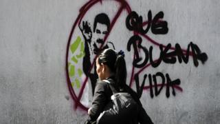 Mulher passa em frente a grafite que retrata Nicolás Maduro