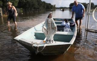 Leigh Babin y su esposo TJ Babin trasladan el barco una estatua de la Virgen María y otros objetos de su casa inundada en Sorrento, Luisiana, EE.UU.