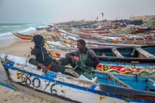 Two men sit together on one of many fishing boats painted in colourful motifs.