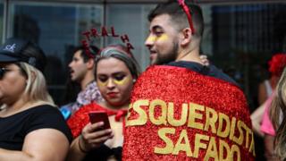 A man wears a cape emblazoned with the phrase "shameless left"