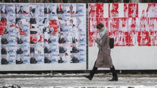 A woman passes a wall showing Moldova election candidates