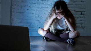 Technology A girl buries her head in her hands in front of a laptop screen in an empty room in this stock image