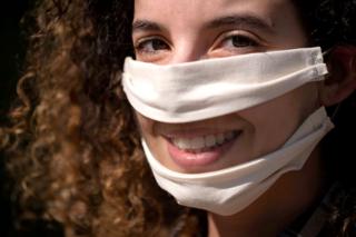 A woman wears a face mask that has a clear plastic panel over the mouth, so the mouth is visible for lip reading