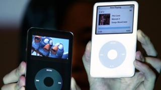 A pair of hands hold two black and white iPod video models - one plays a movie, the other music