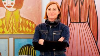 The artist Margo McDaid poses with her paintings at the Helm Gallery in brighton