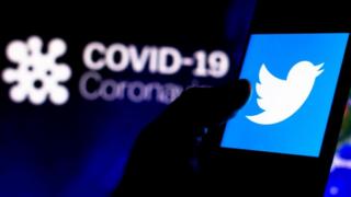 Логотип Twitter на смартфоне с компьютерной моделью коронавируса на заднем плане.