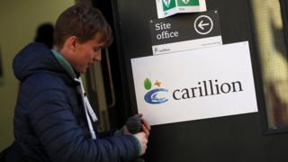 Работник Carillion удаляет знак