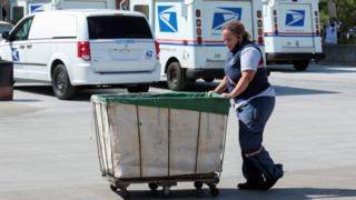 Funcionário do serviço postal dos EUA empurra uma caixa de correio fora de uma agência dos correios em Royal Oak, Michigan (22 de agosto de 2020)