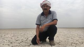 Индийский мужчина в тюрбане становится на колени на потрескавшейся земле, покрытой толстым слоем белой соли