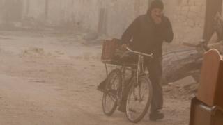 A man covers his face from dust as he walks with a bicycle after a strike on the rebel held besieged al-Shaar neighbourhood of Aleppo, 26 November.