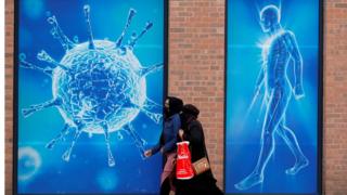 Two women walk past an illustration of a virus in Oldham