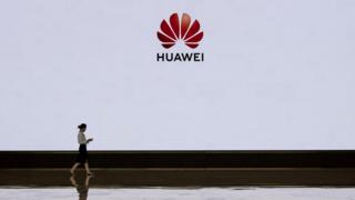 A staff member from Huawei's front desk passes in front of a large screen displaying the logo in the lobby of a building used for high-level client visits and displays on the campus of the company in Bantian on April 12, 2019 in Shenzhen, China.