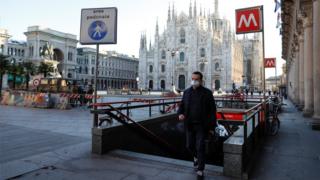 A man wearing a protective face mask walk next to a near-empty Duomo square in Milan