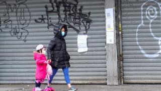 people in masks walk past closed stores