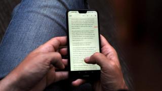 мобилдик телефон аркылуу китеп окуп жатат