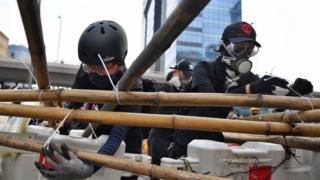 Люди в касках и респираторах связывают бамбуковые шесты