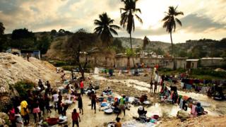 Гаитяне купаются и стирают одежду в потоке в годовщину землетрясения 2010 года