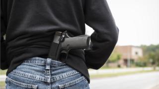 Homem na rua aparece de costas com arma na calça