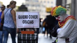 Una persona vestida de payaso pide ayuda para comer