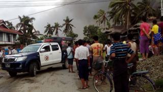 This picture taken on 27 August 2017 shows a police vehicle and people next to houses burnt in Maungdaw township in Rakhine State in Myanmar