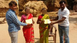 The women accused of being witches, flanked by two men presenting them with ration cards