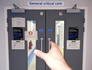 A hand reaches out to open the door of General Critical Care ward in a hospital
