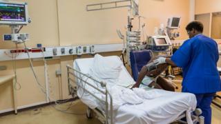 Nurse wey dey help patient for hospital room.