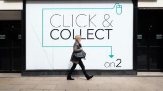 A female pedestrian walks in front of a click-and-collect point on the High Street.