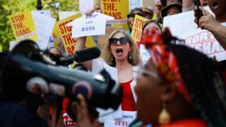 A woman holds a clothes hanger with a sign that says "stop the bans" during a protest against recently passed abortion ban bills at the Georgia State Capitol building