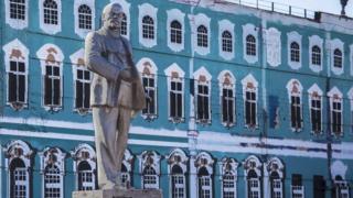 A statue of Lenin stands in front of a painted replica of the Winter Palace in St. Petersburg.
