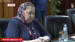 Яха Бексултанова сидит, склонив голову, когда чеченский министр говорит ей извиниться за распространение ложной информации