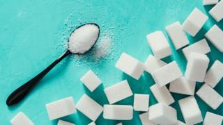 Cubos de açúcar e uma colher cheia com o produto