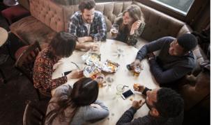 People sit at a pub table with crisps, drinks and phones