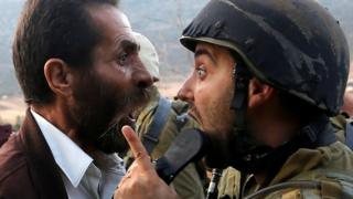 A Palestinian man and an Israeli soldier argue