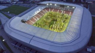 An aerial night shot of the stadium with the forest lit up by flood lighting