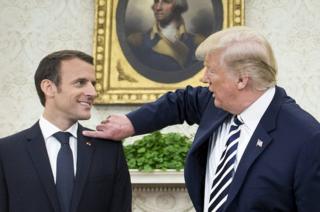 US President Donald Trump (right) pretends to clear dandruff from French President Emmanuel Macron's shoulder in the Oval Office