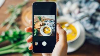 Hand holding a smartphone taking a picture on Instagram of soup