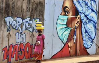 A woman walks past graffiti on a wall depicting hygiene measures to curb the spread of Covid-19 in Conakry, Guinea.