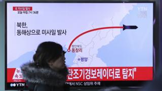 韩国首尔火车站一名女士走过正在播放朝鲜发射导弹报道的电视屏幕(6/3/2017)