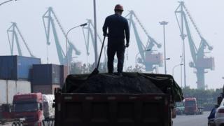 Рабочий загружает уголь в грузовик рядом с контейнерами возле логистического центра недалеко от порта Тяньцзинь на севере Китая, 16 мая 2019 г.