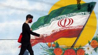 An Iranian boy walks past a mural with Iran's national flag