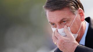 Brazil's President Jair Bolsonaro adjusts his mask as he arrives to a national flag hoisting ceremony