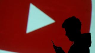 silhouette of a mobile user is seen next to a screen projection of YouTube logo in this picture illustration taken March 28, 2018