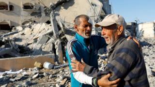 Two men in Khan Younis, Gaza, in front of a destroyed house
