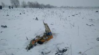На фотографиях с места катастрофы видны обломки самолета на заснеженном поле