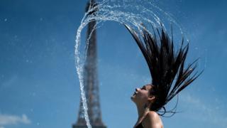 A woman plays the water as she cool herself down in the fountain of the Trocadero esplanade in Paris on June 25, 2019