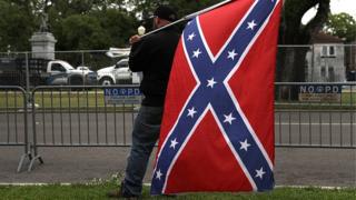 A man holding a Confederate flag across the street from the Jefferson Davis monument in New Orleans, Louisiana