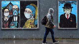 A pedestrian walks past graffiti depicting the subjects within famous artworks, but wearing masks, in Glasgow - 2 September 2020