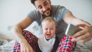 A father takes a selfie with a crying baby