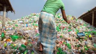 Hombre sobre montaña de botellas de plástico.